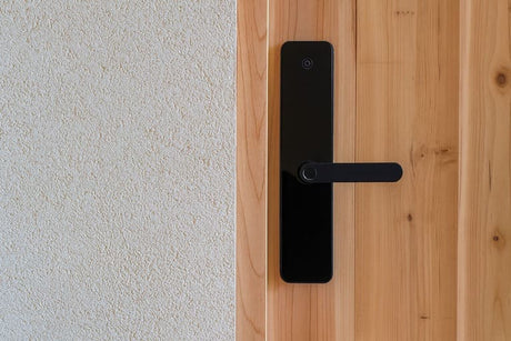 Modern black smart door lock installed on a wooden door next to a textured wall.