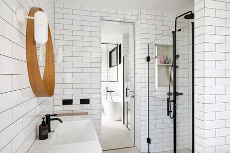 Bathroom with white subway tiles, black-framed glass shower, timber round mirror, and freestanding bathtub.