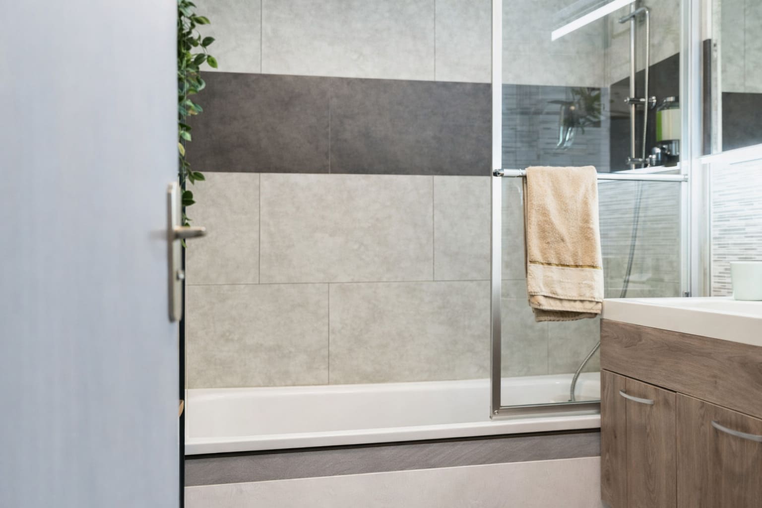 Modern bathroom with a framed glass shower screen, neutral tiled walls, and wood-finish vanity.