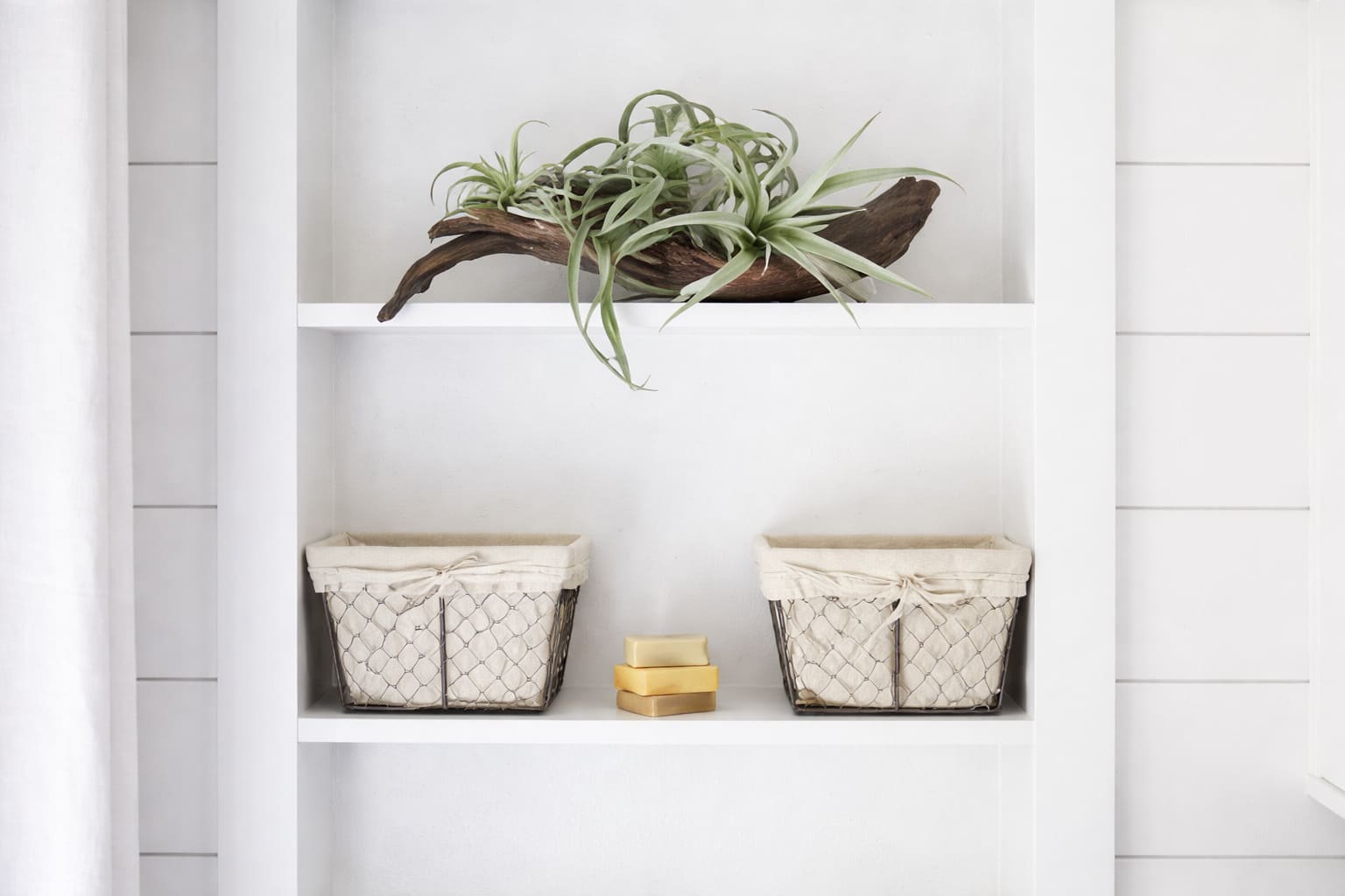 Built-in bathroom shelving with decorative plant, woven storage baskets, and minimalist white cabinetry.