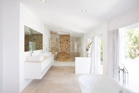 Bright modern bathroom with double vanity, walk-in glass shower, stone feature wall, and freestanding bathtub.