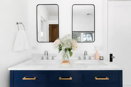 Modern bathroom with navy double vanity, white quartz countertop, chrome tapware, and twin black-framed mirrors.