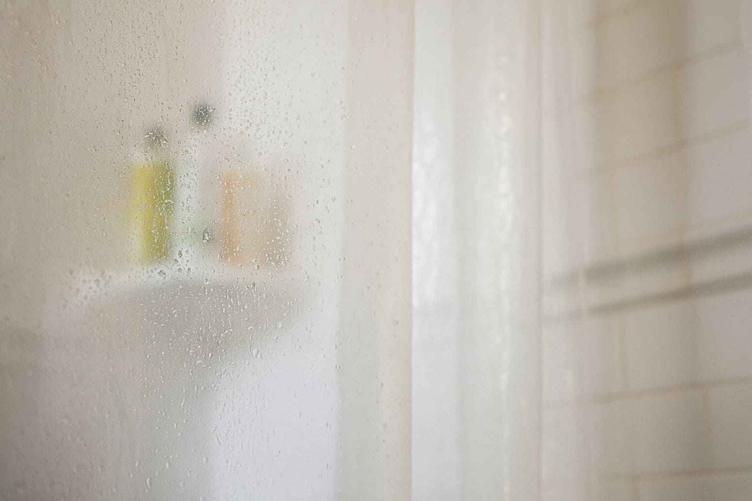 Foggy shower glass with water droplets and blurred shampoo bottles in the background.