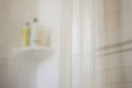 Foggy shower glass with water droplets and blurred shampoo bottles in the background.