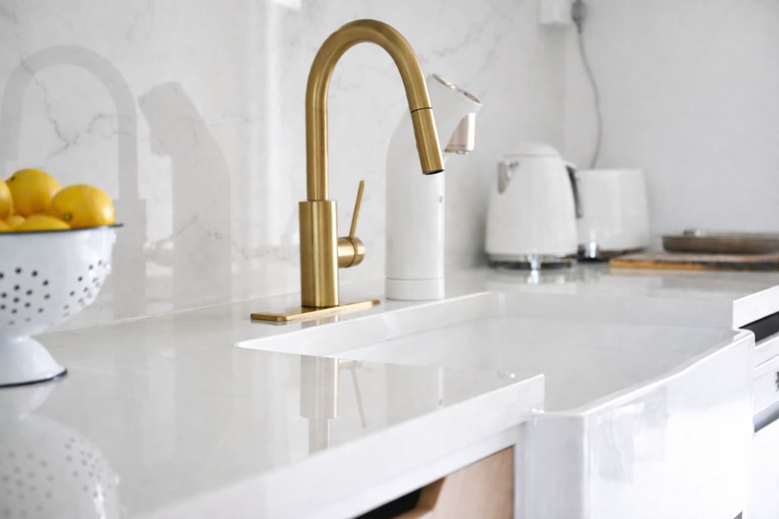 Modern kitchen sink with brushed brass mixer tap, white benchtop, and minimalist countertop accessories.
