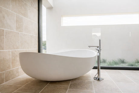 Modern bathroom featuring a freestanding white oval bathtub and stainless steel faucet, illuminated by natural light through large windows.