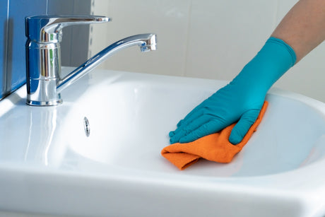 Cleaning bathroom vanity sink with cloth as part of daily care and maintenance.