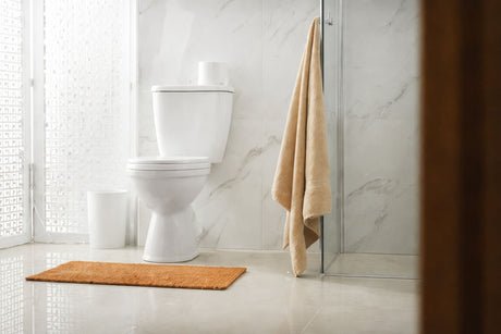 Modern white ceramic toilet in marble bathroom with beige towel and bath mat