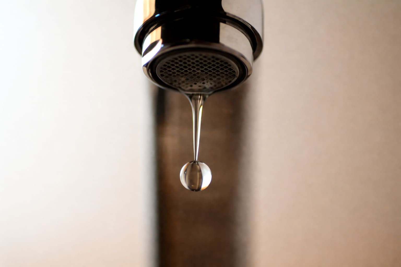 Close-up of a chrome faucet with a single water droplet forming at the spout, highlighting clean water flow.