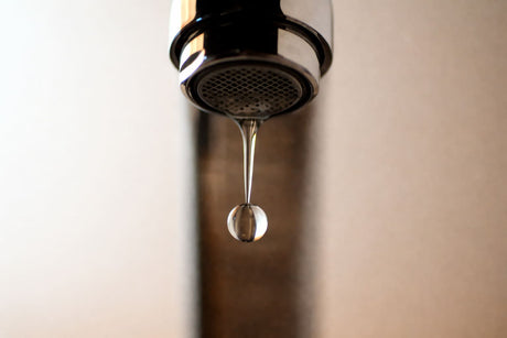 Close-up of a chrome faucet with a single water droplet forming at the spout, highlighting clean water flow.
