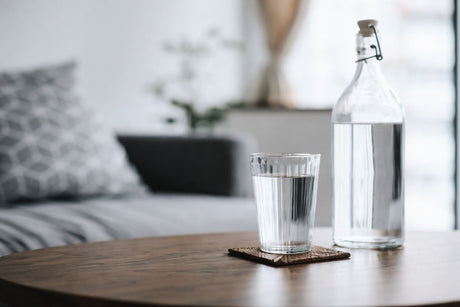Table with glass of water, clear bottle, wooden surface, and soft natural light.