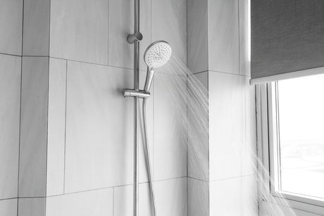 Handheld shower spraying water in a tiled bathroom
