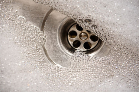Close-up of stainless steel sink drain with soap bubbles and flowing water during cleaning.