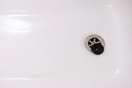 White bathtub with stainless steel drain and black rubber plug in a clean modern bathroom.