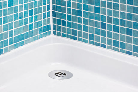 Shower base with stainless steel drain and blue mosaic tile walls in a modern bathroom.