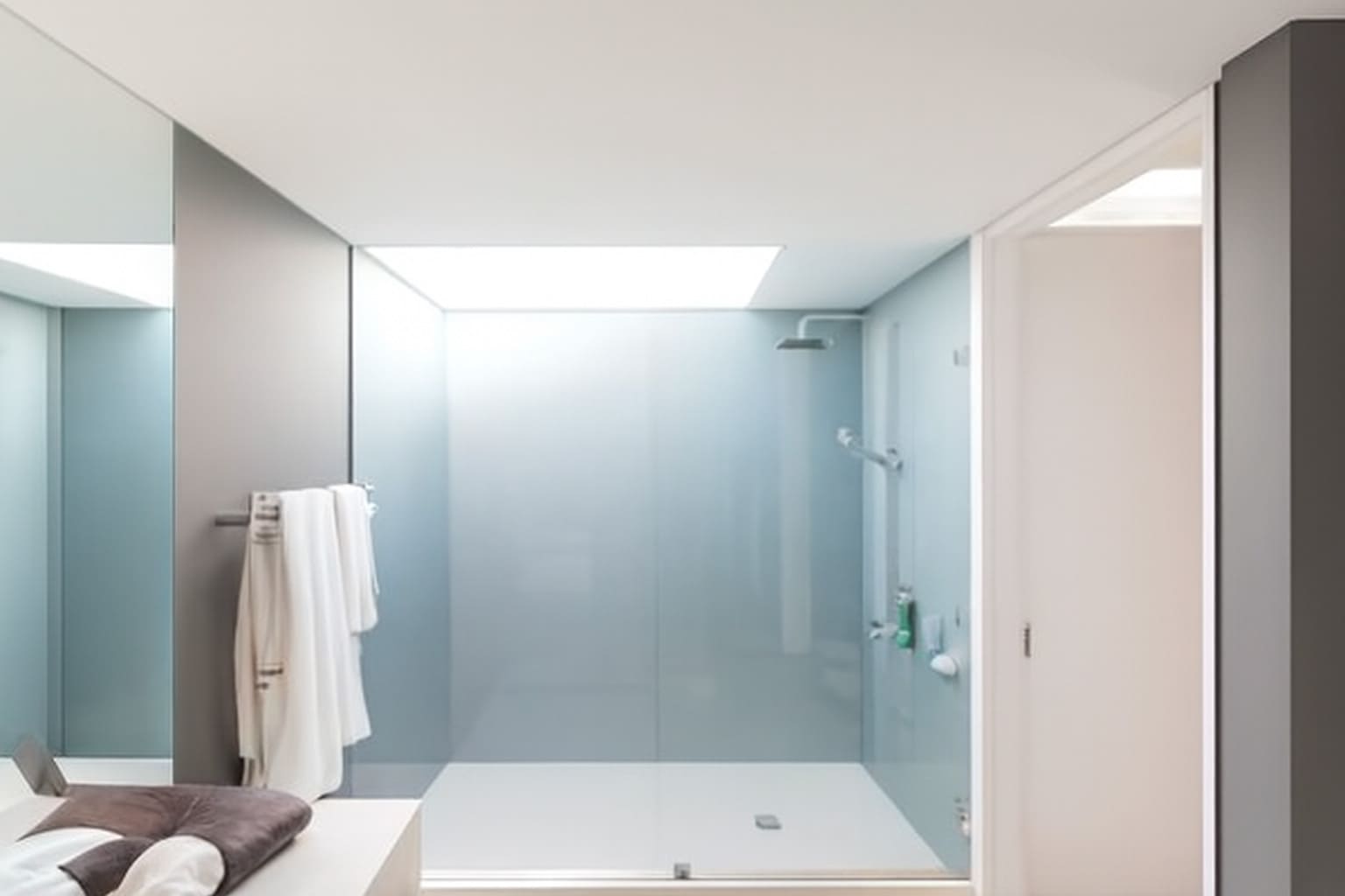 Modern minimalist bathroom with frameless walk-in shower, plush towels, and natural light.