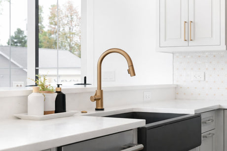 Modern kitchen with brushed brass mixer tap, black farmhouse sink, white benchtop, and bright natural light.