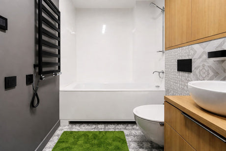 A modern bathroom featuring a sleek white bathtub, a green bath mat, and a wooden vanity with a white vessel sink and geometric backsplash.