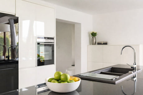 A kitchen with white cabinetry, black island benchtop, undermount sink, and chrome mixer tap.