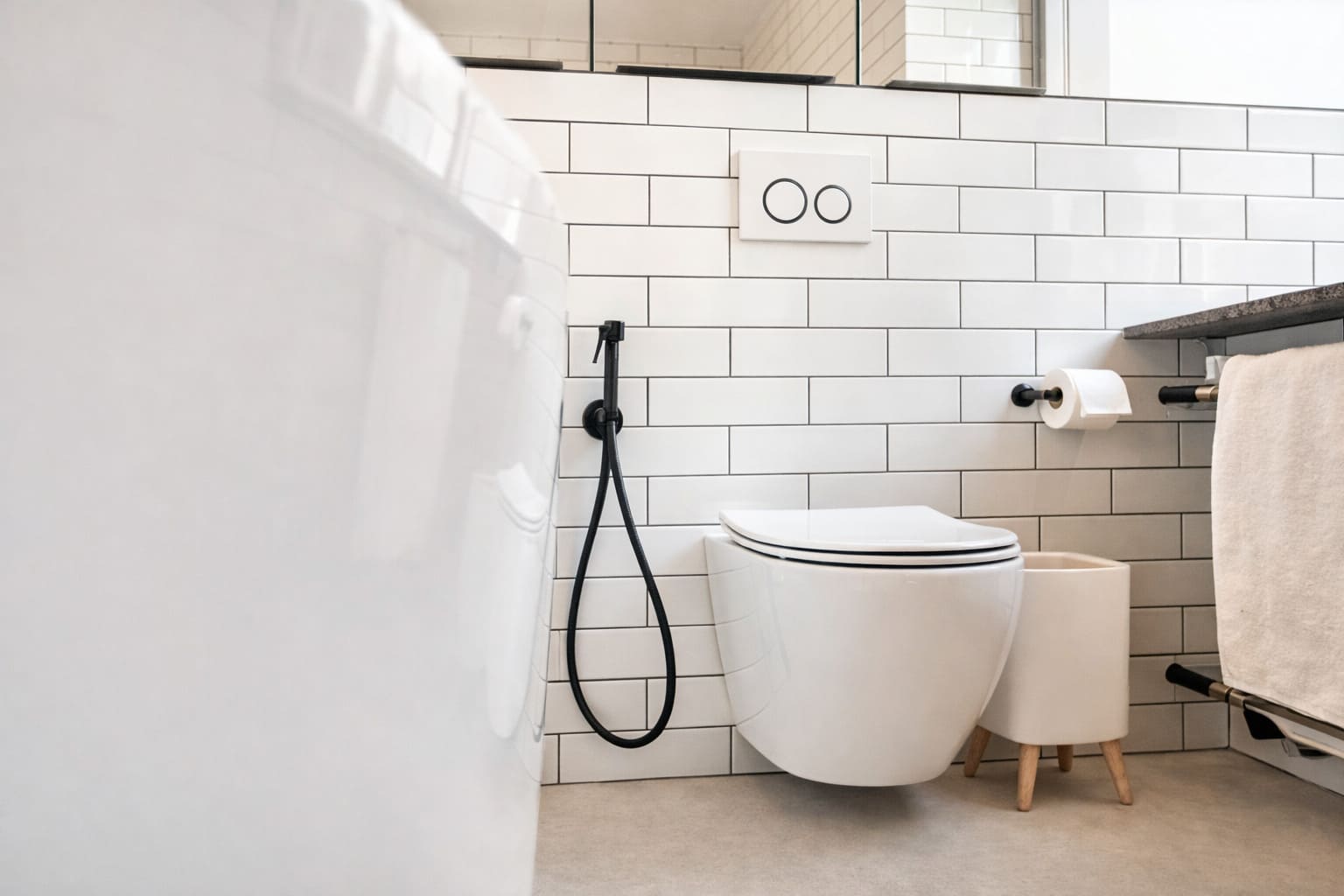 Modern bathroom with wall-hung toilet, concealed cistern flush plate, white subway tiles, and black bidet spray.