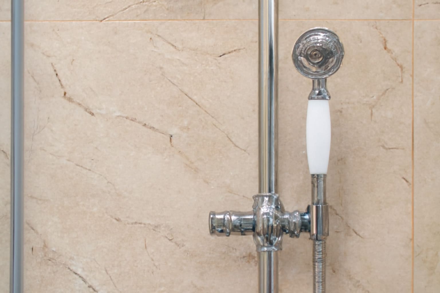Vintage chrome handheld showerhead against beige marble wall