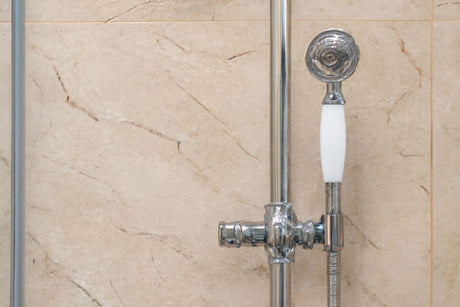 Vintage chrome handheld showerhead against beige marble wall