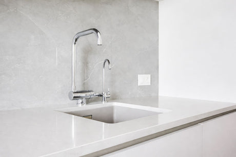 Modern kitchen sink with chrome mixer tap, undermount basin, and light grey stone splashback.