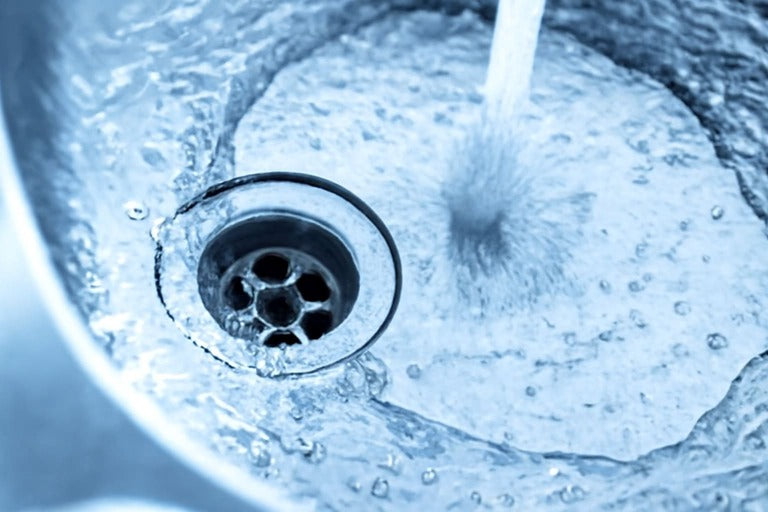 Close-up of water flowing into a stainless steel sink with a visible drain.