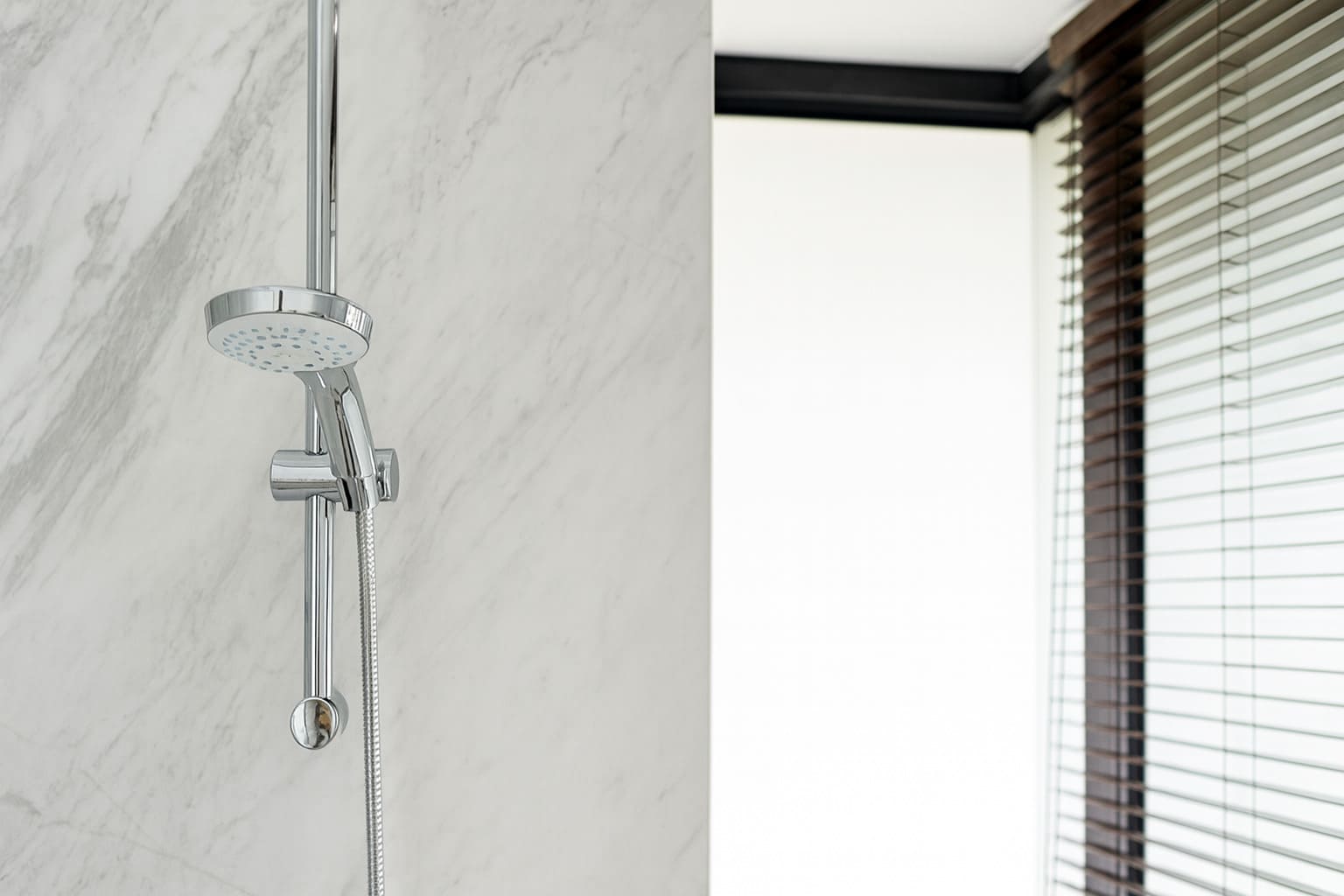 Chrome handheld shower on marble wall in a modern bathroom