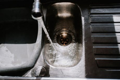 Close-up of water flowing from a faucet into a stainless steel sink, creating ripples and bubbles.