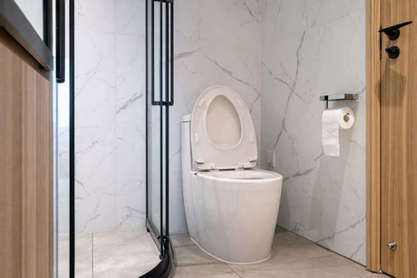 Modern white toilet with open lid in a minimalist bathroom featuring marble-look wall tiles, black-framed glass shower screen, and wooden accents.