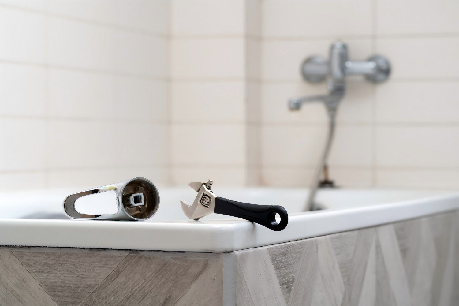 Bathroom tap repair with removed handle and adjustable wrench beside a bathtub.