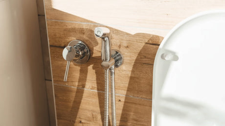Chrome bidet spray next to toilet on wood-look wall