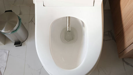 Overhead view of white smart toilet with bidet wand on marble floor