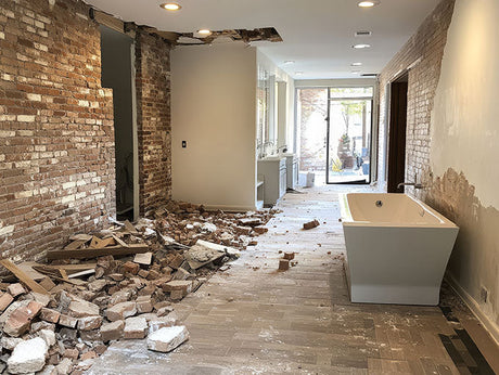 Bathroom renovation in progress with exposed brick wall, construction debris, and new freestanding bathtub