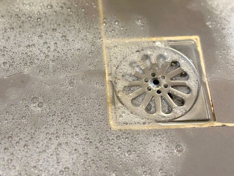 Bathroom floor drain with soap bubbles during cleaning to remove odours and buildup.