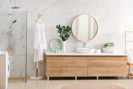 Round timber-framed mirror above wooden vanity in marble-tiled bathroom