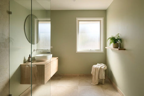 Sage green bathroom with timber floating vanity, round mirror and glass shower screen