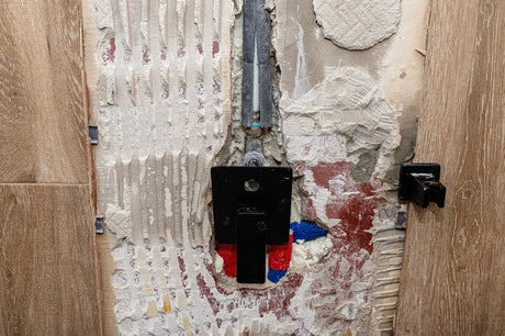 Exposed bathroom wall with plumbing pipes and black tap valve bracket