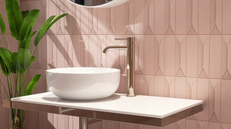 White vessel sink with chrome faucet, pink tile backsplash, and green plant.