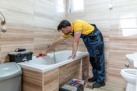 Plumber in yellow shirt using red spanner to install bathtub tap