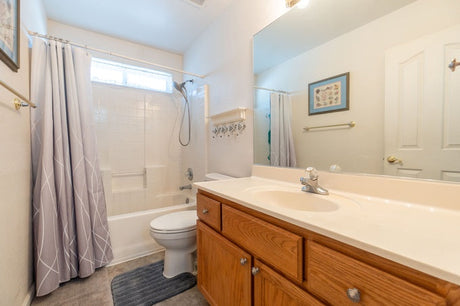 Bathroom with wood vanity, tub shower, toilet, large mirror, and gray shower curtain