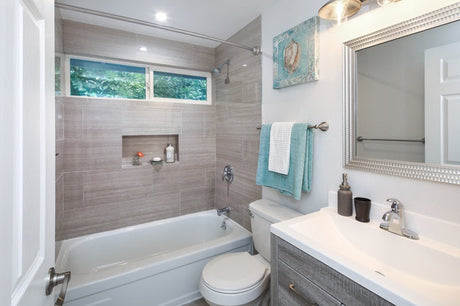 Bathroom with tub shower, gray tile surround, toilet, vanity, and blue towels.