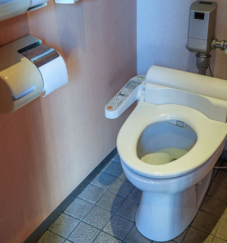 Japanese smart toilet with bidet control panel beside triple toilet paper dispensers