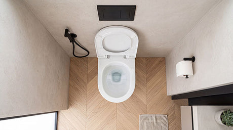 Overhead view of white wall-hung toilet with bidet hose on herringbone timber floor