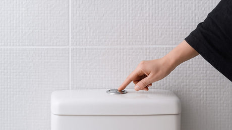 A hand is pressing the toilet flush button
