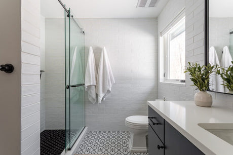 Bright modern bathroom with glass walk-in shower, white subway tile walls, patterned floor and natural light