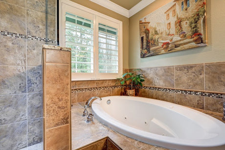 Built-in spa bath with stone tiles, chrome taps and plantation shuttered window