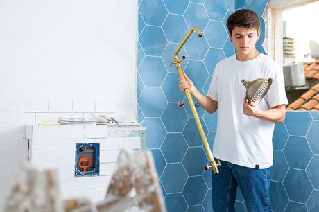 Young man holding brass shower arm and head in a bathroom under renovation