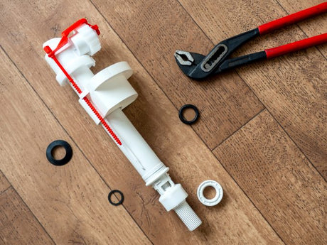 Toilet cistern inlet valve and repair tools laid out on a wooden floor ready for installation